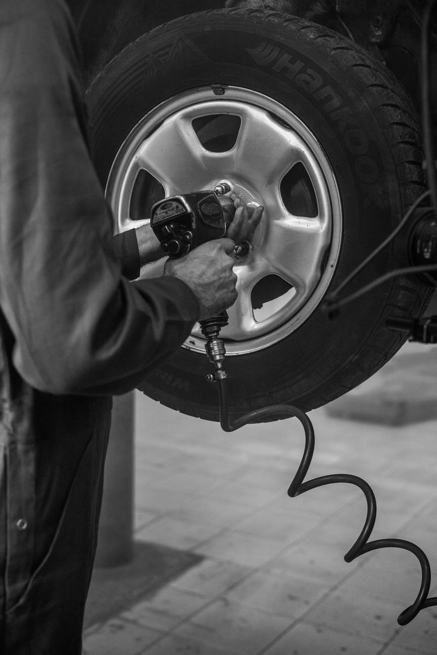 grayscale photo of person changing car tire with an air wrench